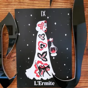 Affiche A4 du tarot L’Ermite, illustration pop folk ésotérique en noir, rouge et blanc, représentant une silhouette drapée tenant une lanterne, accompagnée d’un chat noir.