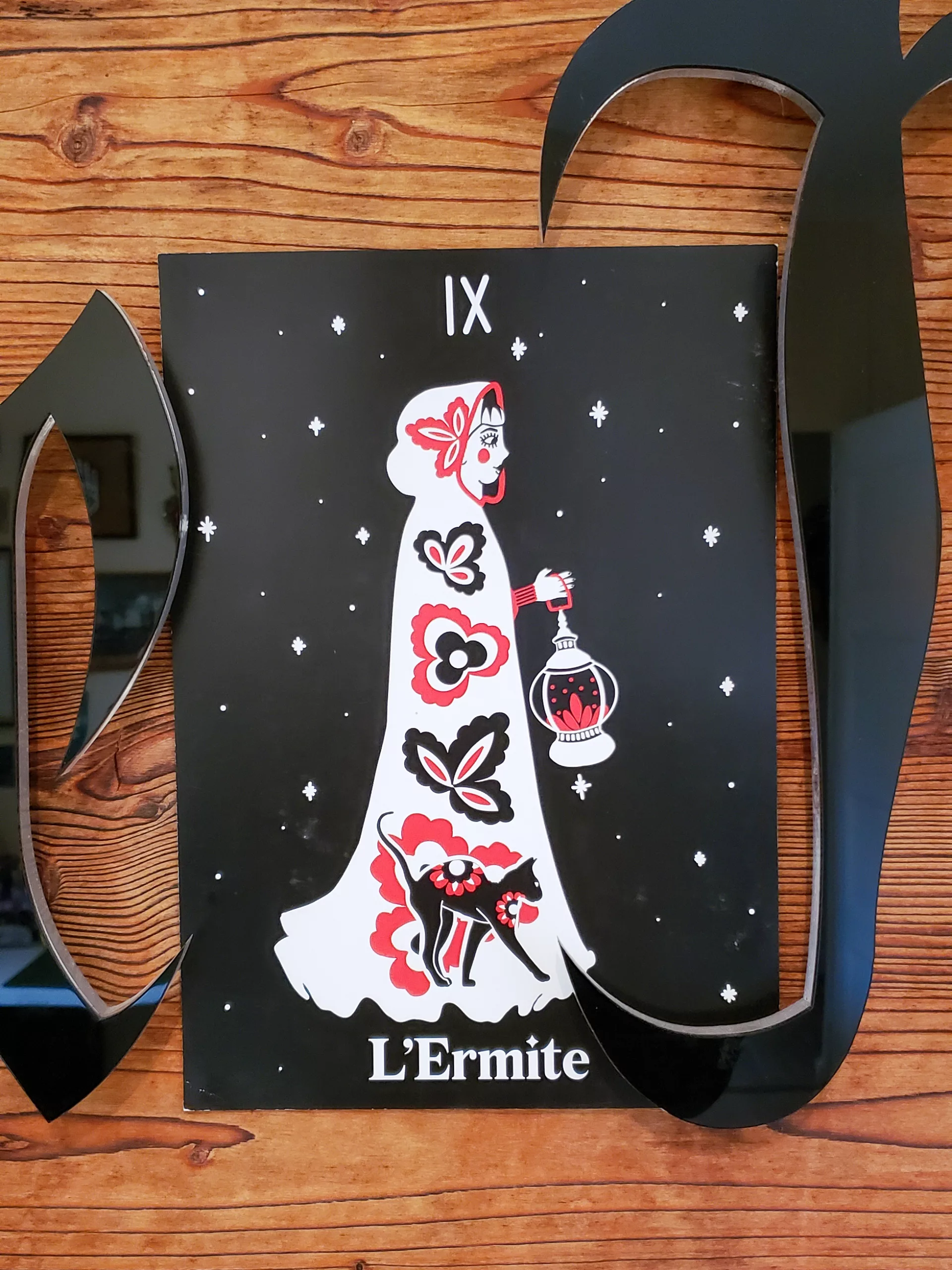 Affiche A4 du tarot L’Ermite, illustration pop folk ésotérique en noir, rouge et blanc, représentant une silhouette drapée tenant une lanterne, accompagnée d’un chat noir.