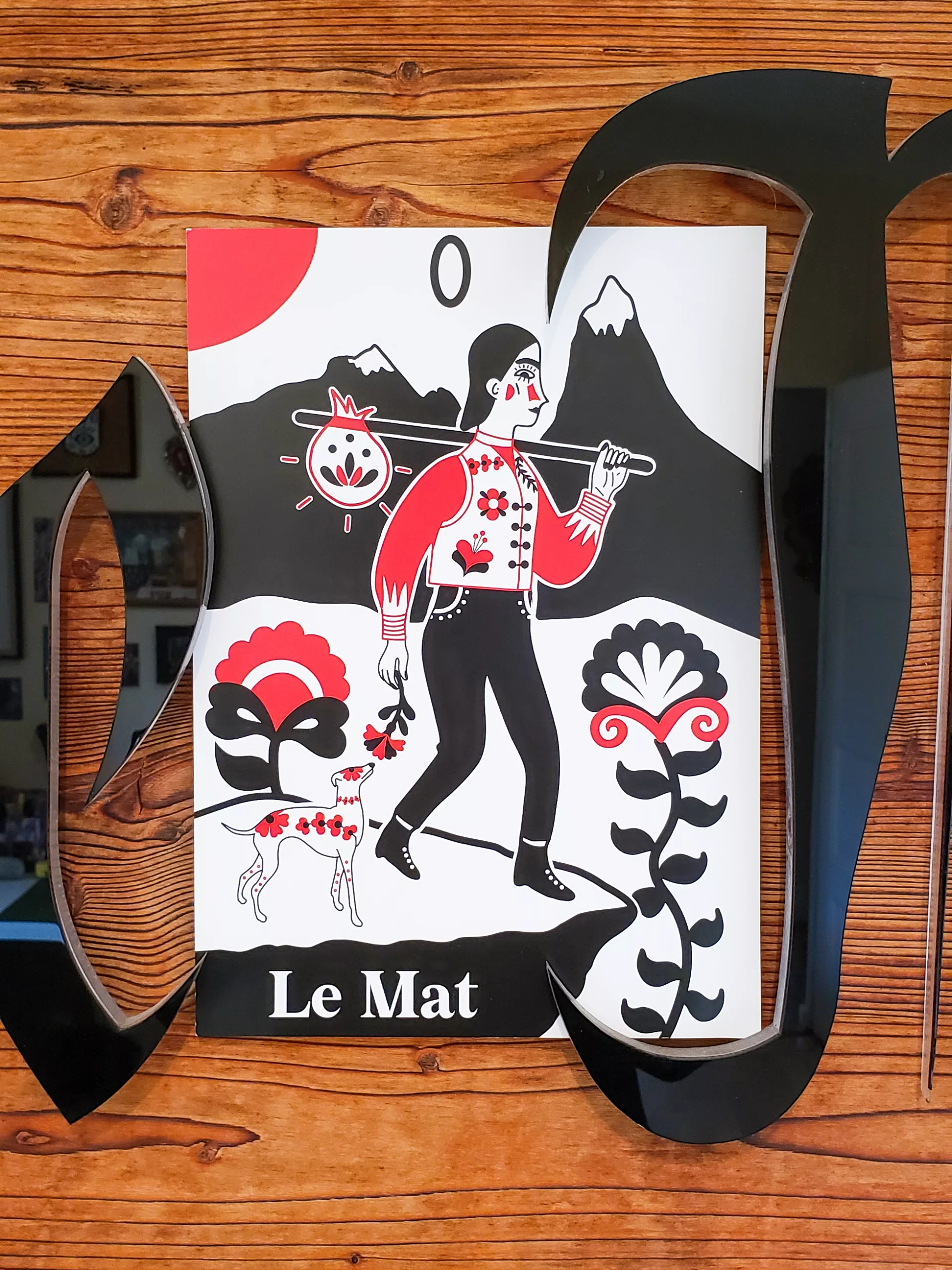 Affiche A4 du tarot Le Mat, illustration pop folk ésotérique en rouge, noir et blanc, représentant un voyageur et son chien au milieu de fleurs et montagnes.