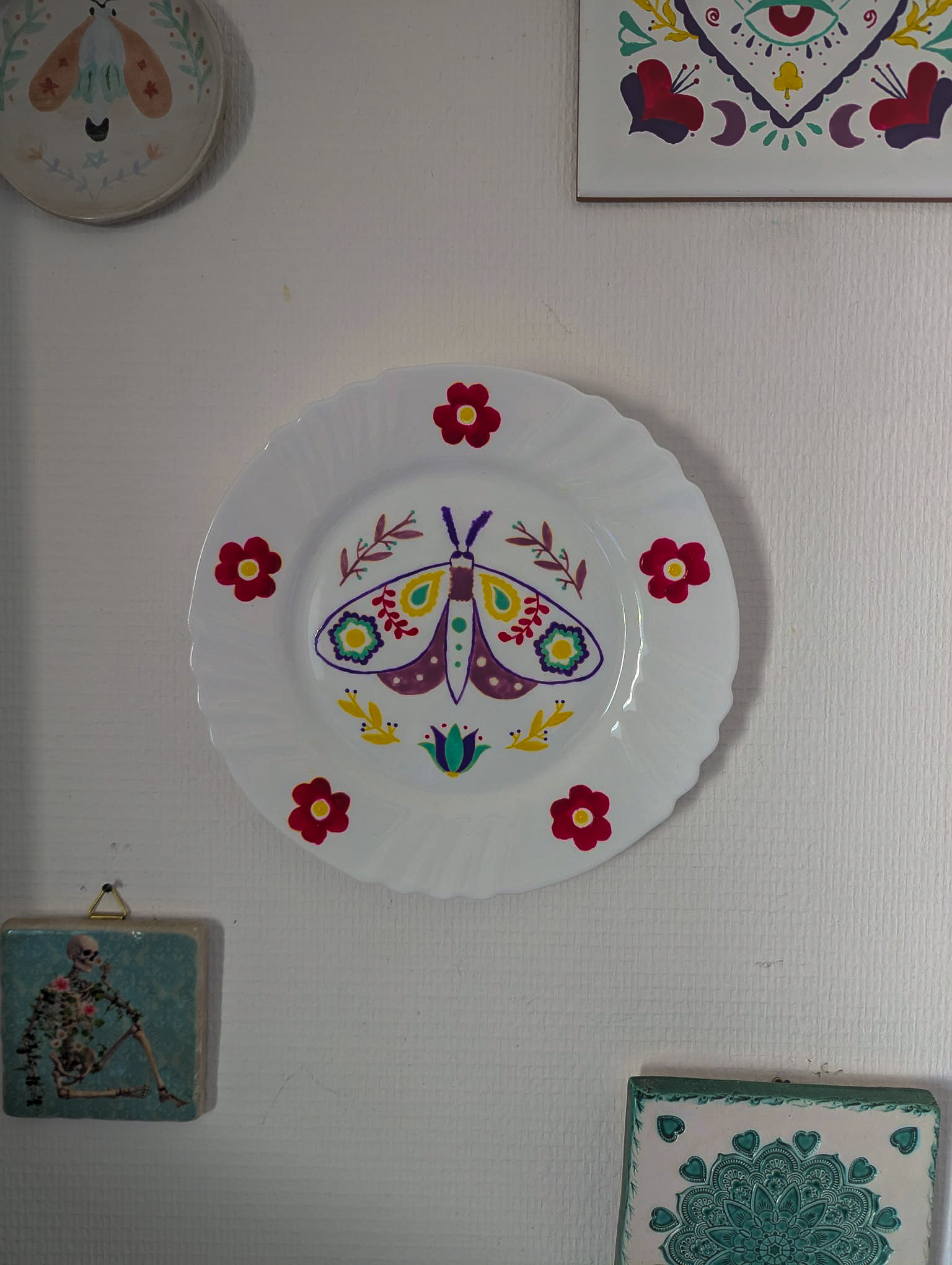 Assiette murale en porcelaine peinte à la main, papillon folk multicolore entouré de fleurs rouges, Fortunae Studio